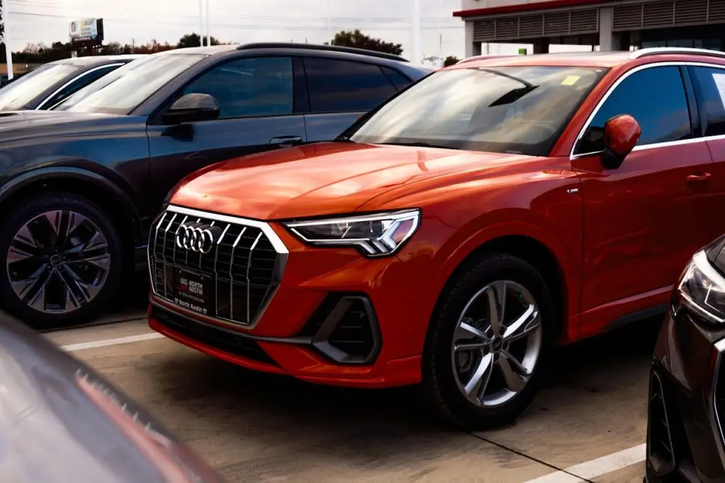 A vibrant orange SUV parked among other vehicles at a car dealership, showcasing modern car design.